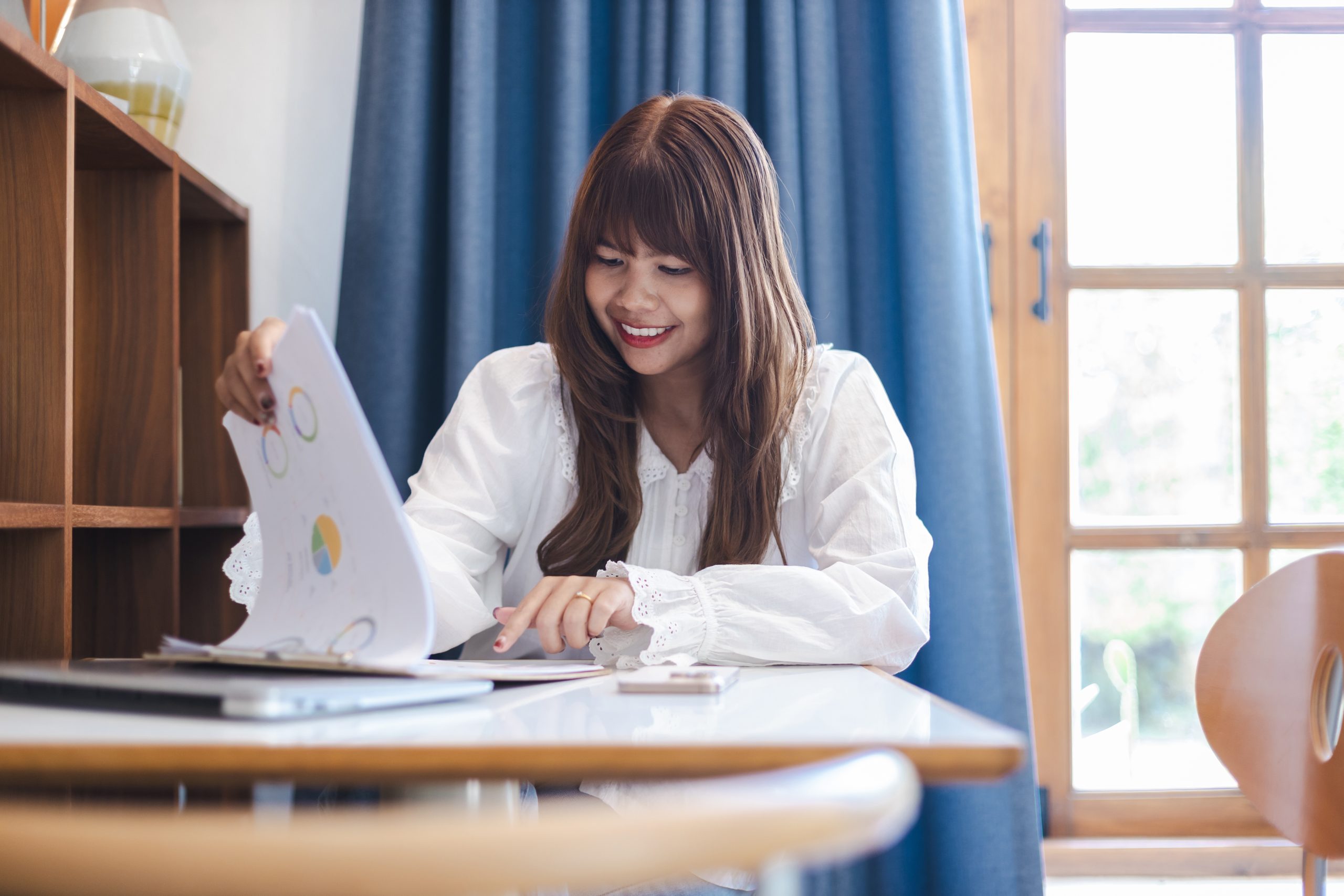 Small business owner reviewing performance charts and analytics documents at a desk, evaluating the timeline of her SEO progress.