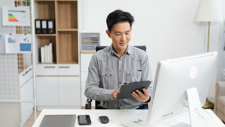 Mature small business owner sitting at a laptop in his office, thinking through a strategy decision about outsourcing.
