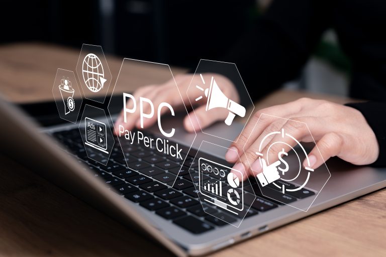 Workspace concept of pay-per-click advertising campaign planning: a person at a laptop with bright virtual icons of ad megaphones, target audience, budget click, and performance analytics floating above the desk.