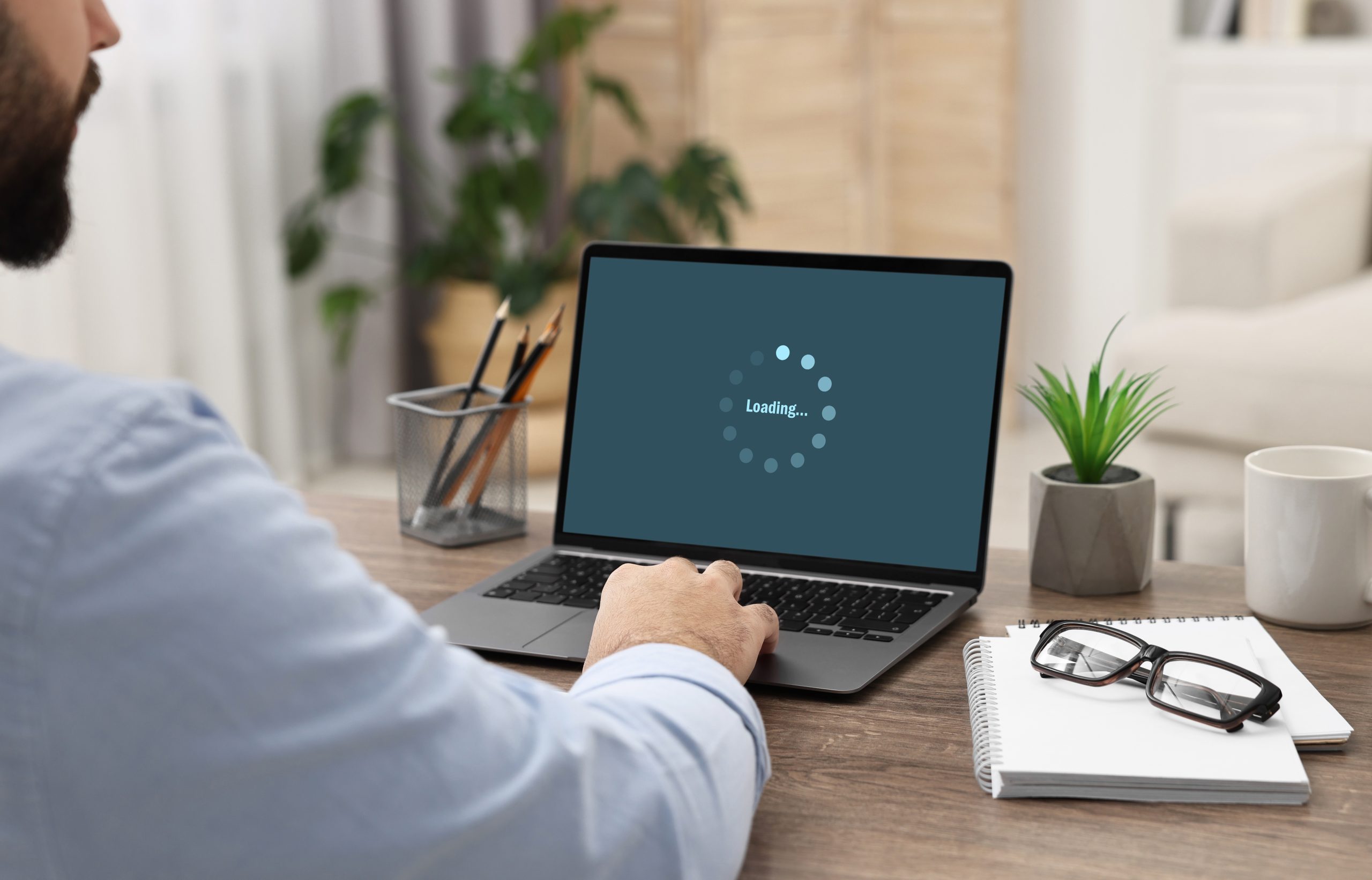 Small business owner working on a laptop showing a slow loading spinner on the website screen at a wooden desk.