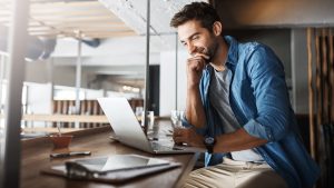 Small-business owner sitting with a laptop in a cafe, thoughtfully reviewing his business online