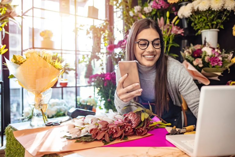 Florist shop owner at her counter holding a phone with an open laptop beside her