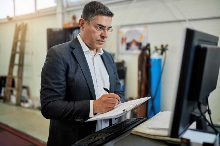Service business owner writing on a clipboard beside the shop computer counter