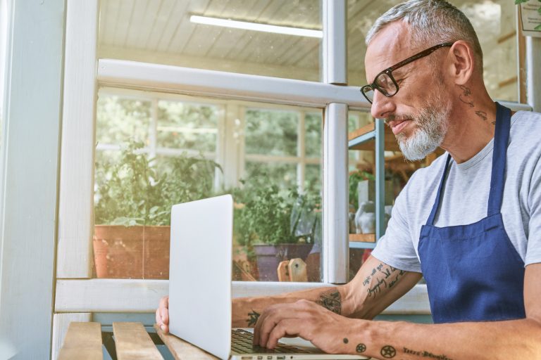Small business owner in an apron checking his laptop at the counter of his shop