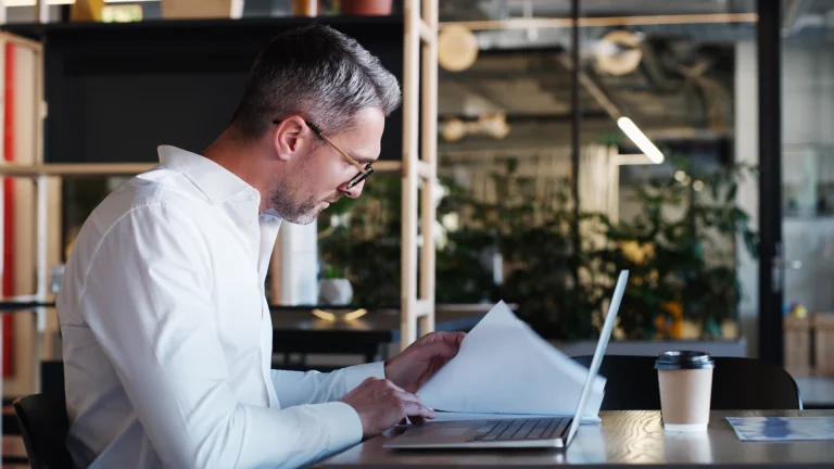 Businessman reviewing printed documents at his laptop in a modern office