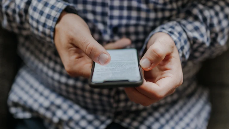 Person in a checked shirt holding a smartphone with text on its screen