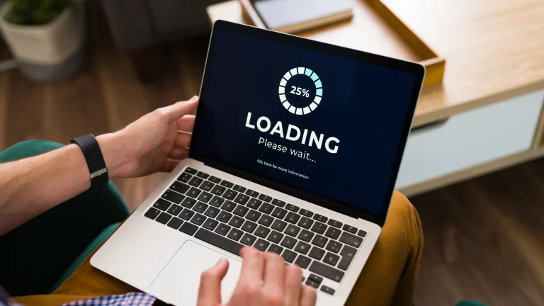 Laptop on a person's lap displaying a 25 percent loading indicator and Please wait message