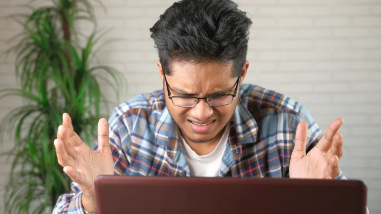 Frustrated man throwing up his hands at his laptop screen