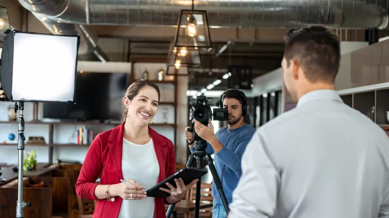 Camera operator filming a woman with a tablet talking with a man indoors