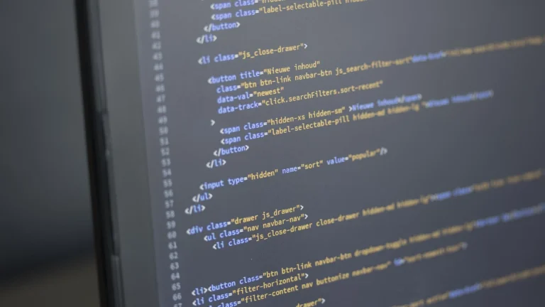 A close-up of lines of HTML code in blue, orange and white on a dark computer monitor, photographed at an angle